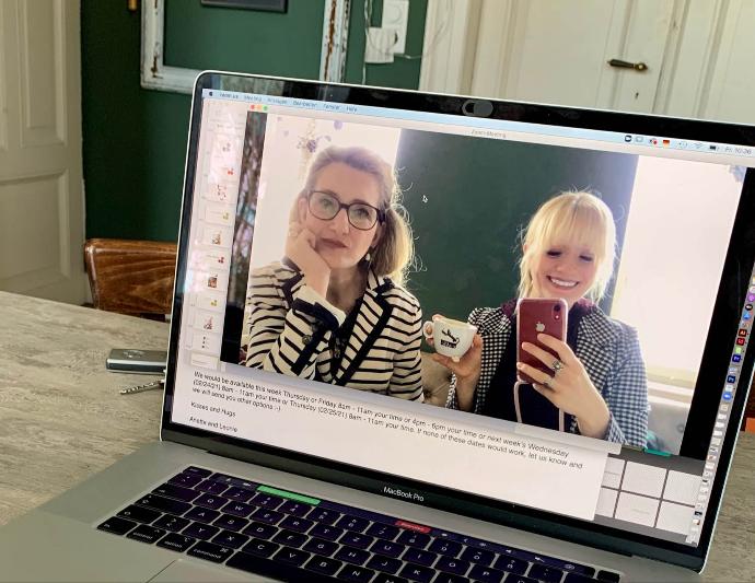  two women taking a mirrored selfie in their MacBook with their FaceTime camera. One of them is holding a  cappuccino cup.