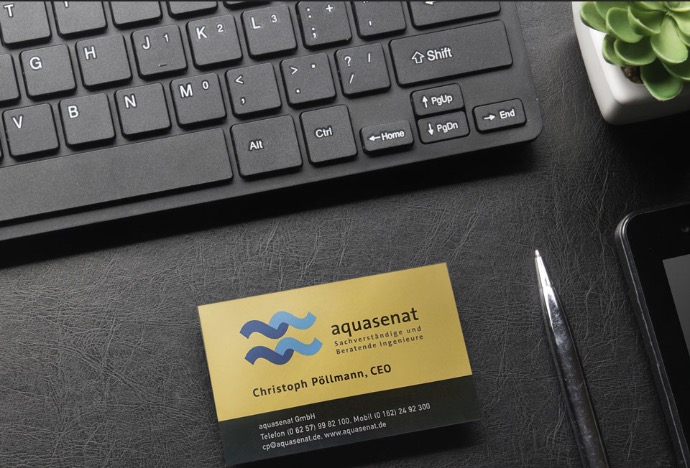 bird's eye view of a black leather look desk with a black keyboard, a cut cactus, and a golden business card