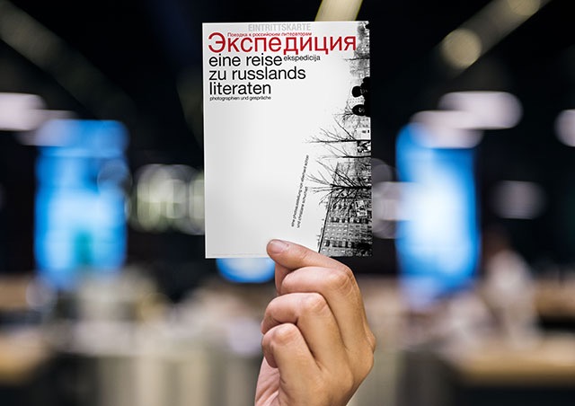 hand holding the ekspedicija postcard in front of a blurred background